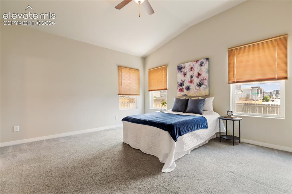 Image 16 of 29: primary bedroom features vaulted ceilings, a ceiling fan and window coverin