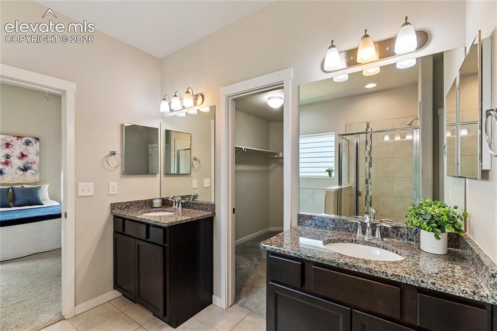 Image 18 of 29: Primary bathroom features dual sinks, a walk-in closet, sold granite counte