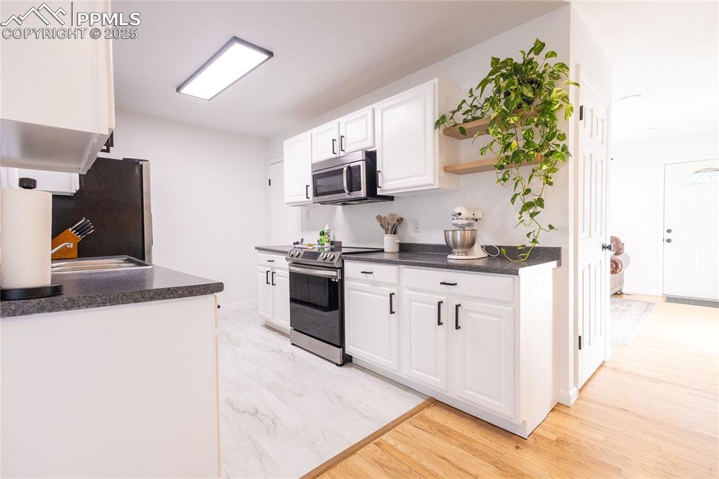 Image 4 of 27: Kitchen featuring white cabinets, dark countertops, stainless steel applian