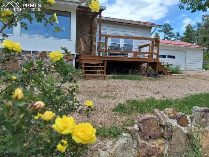 Image 21 of 30: Rear view of house with a wooden deck, stairway, stone siding, and a garage