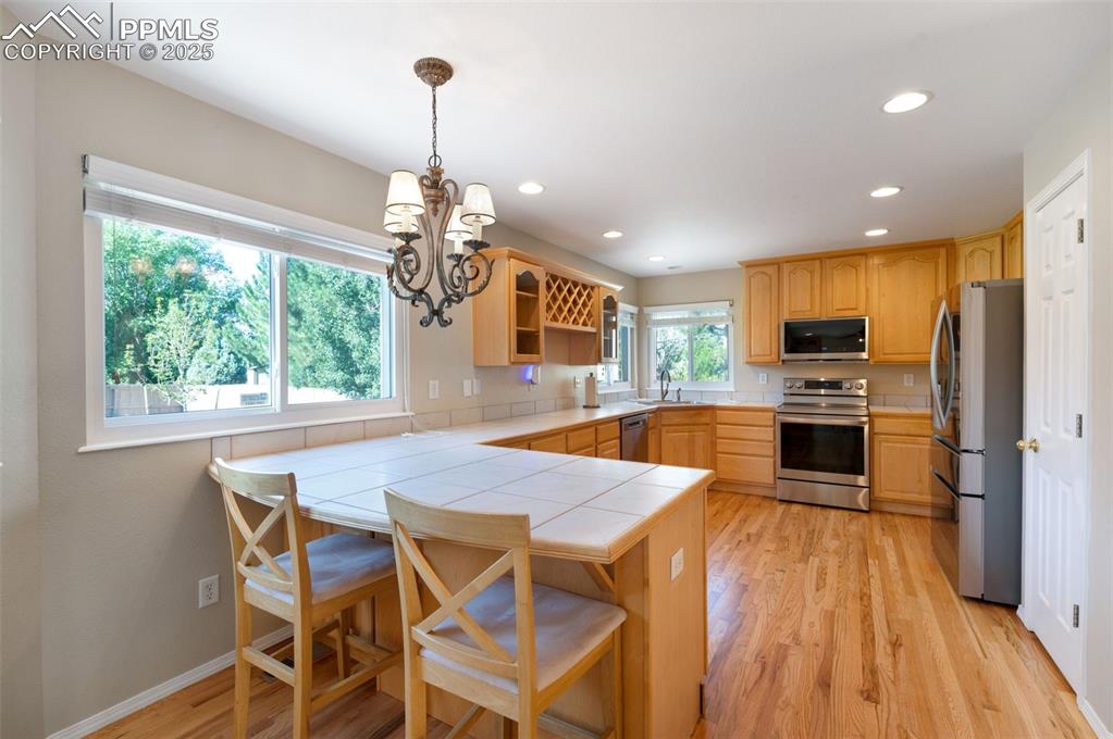Image 8 of 37: Kitchen with tile countertops, stainless steel appliances, decorative light