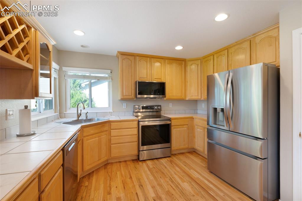 Image 9 of 37: Kitchen with stainless steel appliances, light wood-type flooring, tile cou