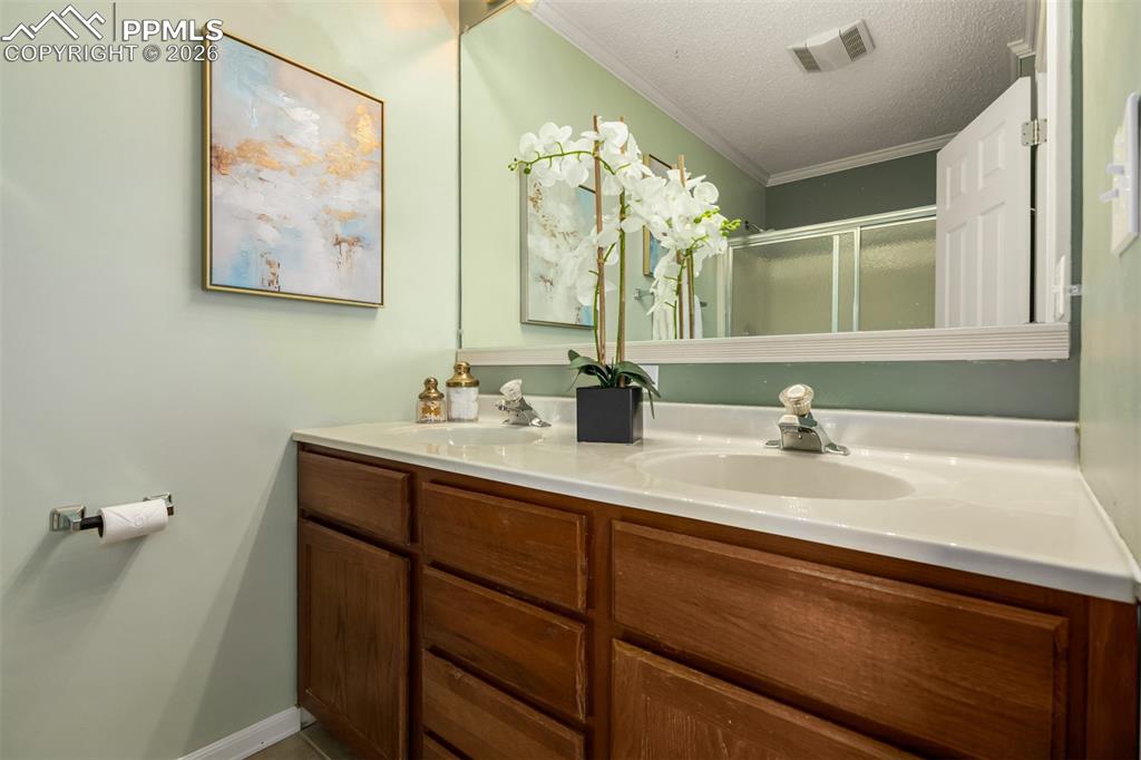 Image 16 of 30: Bathroom with double vanity, a textured ceiling, ornamental molding, and a 