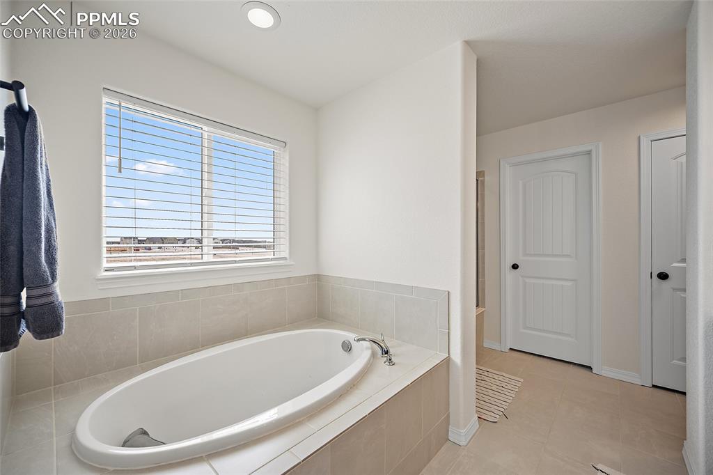 Image 28 of 45: Large soaking tub with tiled surround, framed by a wide window with horizon