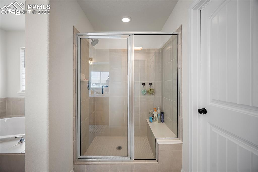 Image 29 of 45: Glass-enclosed walk-in shower featuring light-toned tile, a built-in bench,