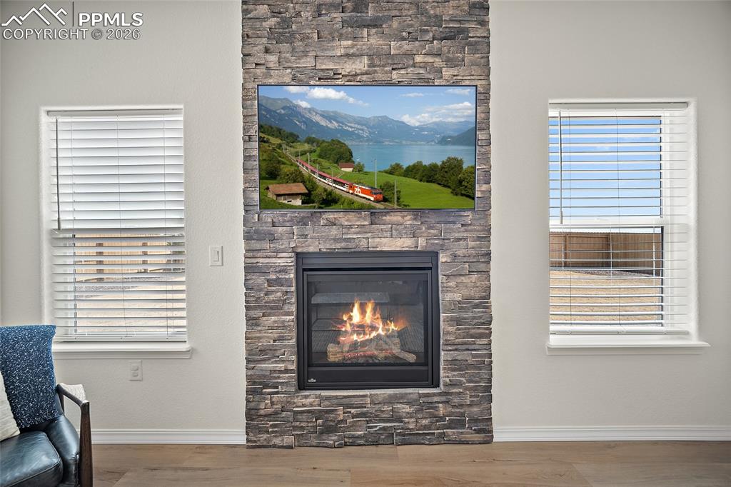 Image 9 of 45: Stacked stone fireplace with a black firebox, flanked by two windows with w