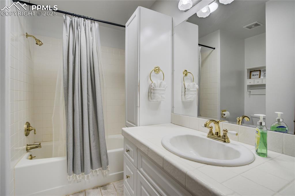 Image 19 of 50: 2nd bathroom with shower/bath combo, shower curtain, vanity, storage closet