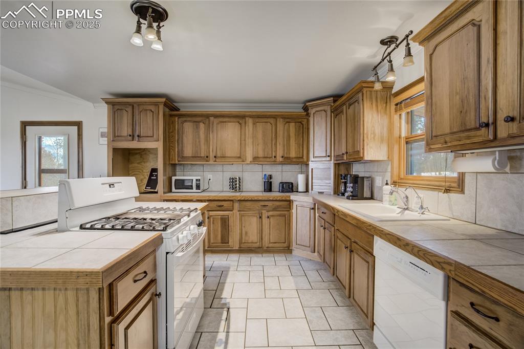 Image 4 of 50: Kitchen featuring tile counters and backsplash, refrigerator, propane gas s