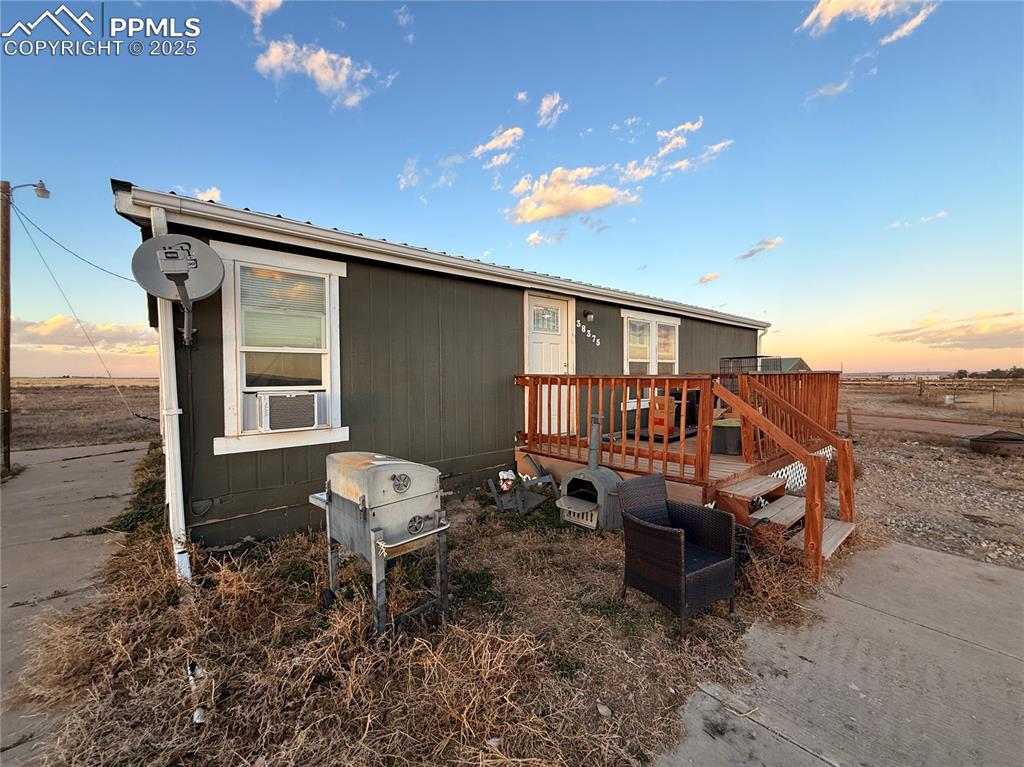 Caption: Back of house at dusk with a wooden deck, a metal roof, and cooling unit