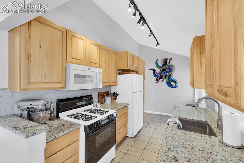 Image 16 of 50: Kitchen featuring white appliances, light brown cabinetry, decorative backs