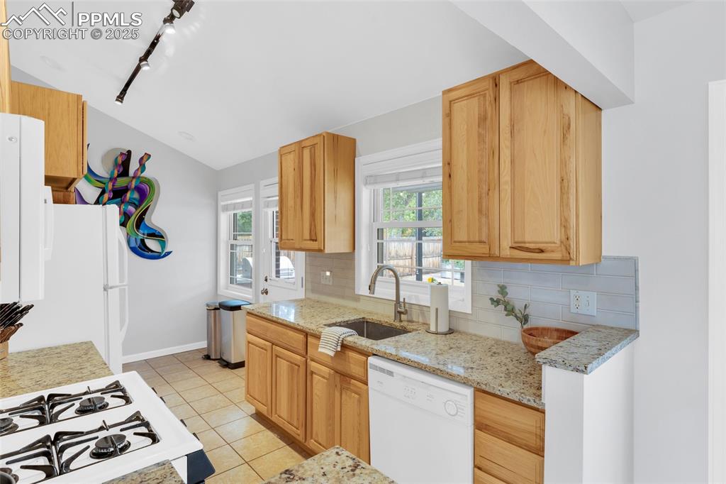 Image 17 of 50: Kitchen featuring white appliances, decorative backsplash, light tile patte