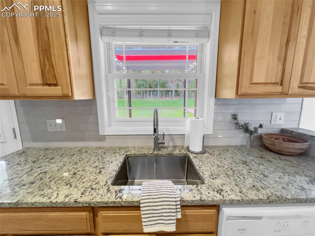 Image 35 of 50: Kitchen view of white dishwasher, backsplash, and light stone counters