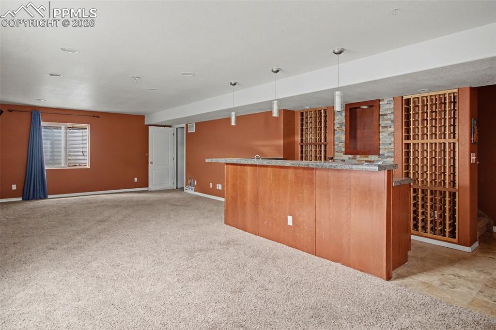 Image 28 of 33: Kitchen featuring light colored carpet, hanging light fixtures, dark stone 