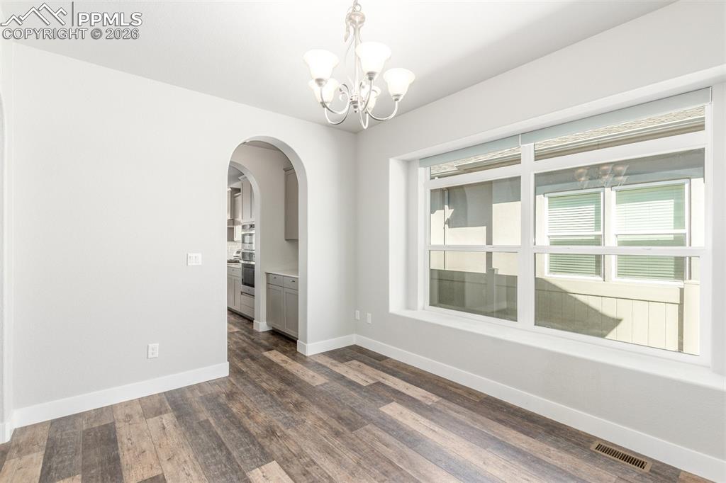 Image 15 of 46: Empty room with arched walkways, dark wood-style flooring, and a chandelier