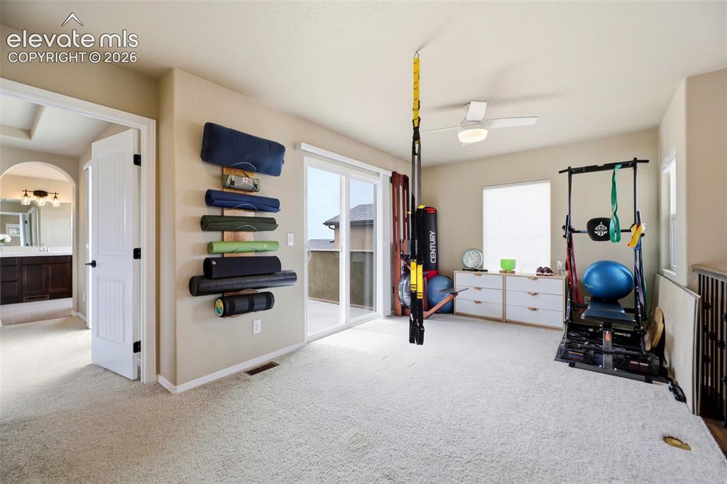 Image 26 of 48: Carpeted loft being used as an exercise room, with a ceiling fan, sliding g