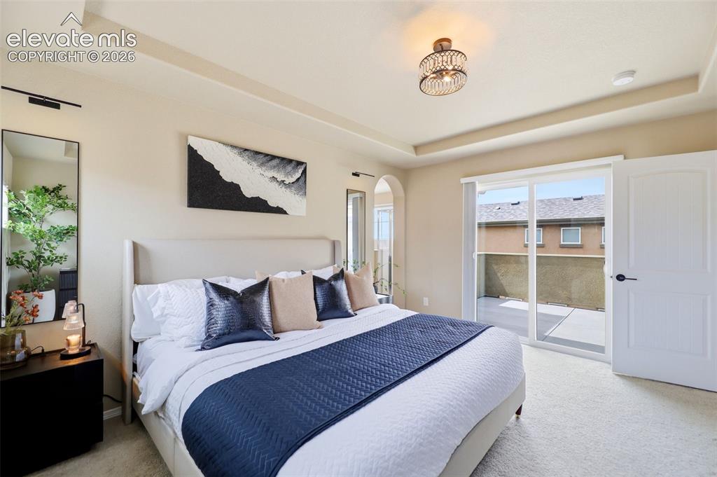 Image 30 of 48: Tray ceiling, carpeted flooring, arched doorway, sliding glass door leading