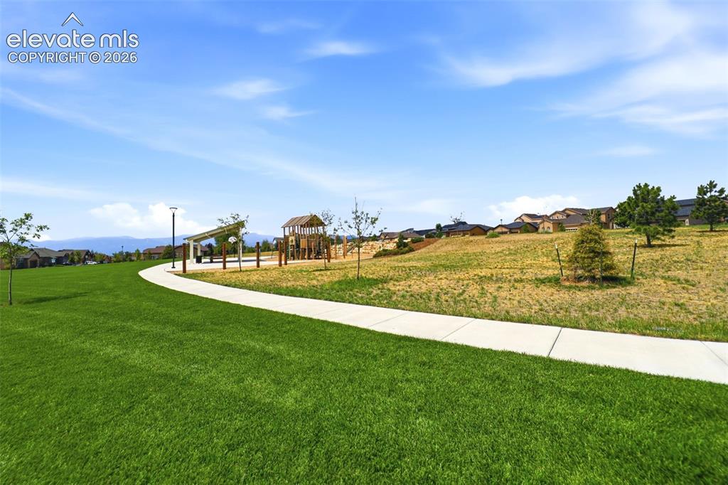 Image 36 of 48: Expansive green space featuring a paved walkway, mature trees, a covered pe