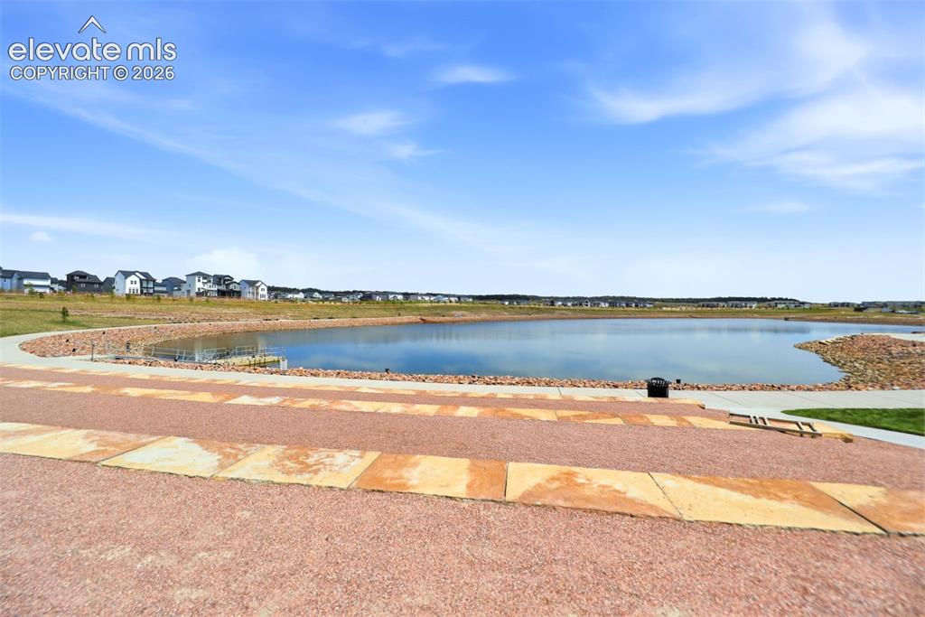 Image 39 of 48: Paved pathways surround a calm lake, bordered by a landscaped rock embankme