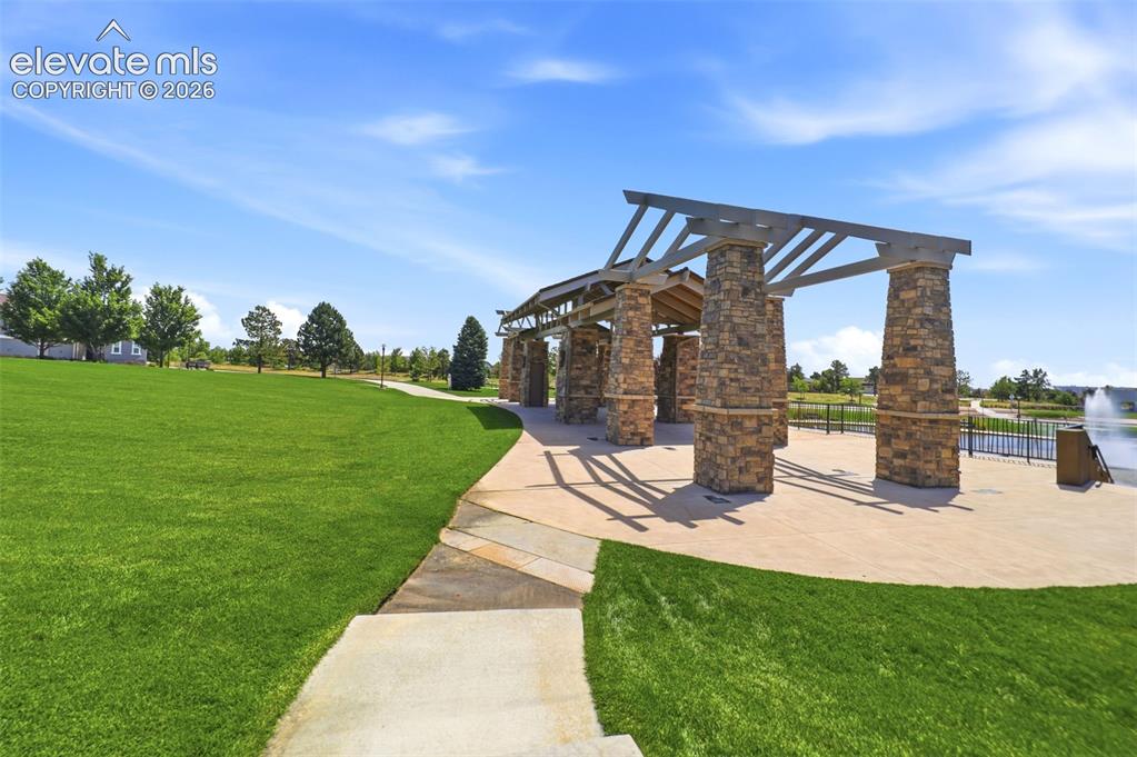 Image 42 of 48: Expansive green space featuring a stone and wood beam pergola, a paved pati