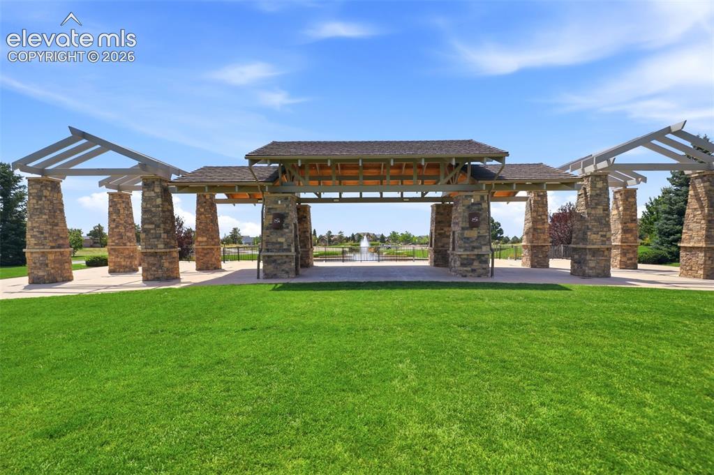 Image 44 of 48: Expansive green space featuring a stone and wood beam pergola, leading to a