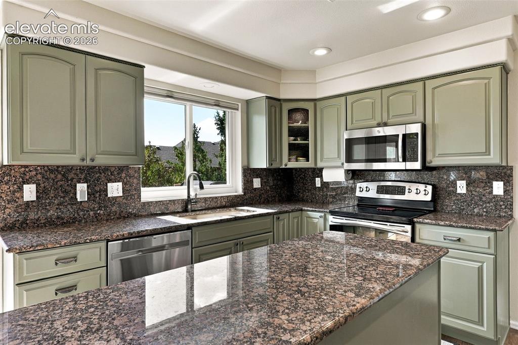 Image 14 of 50: Expansive kitchen featuring a large island, wood cabinetry, stone counterto