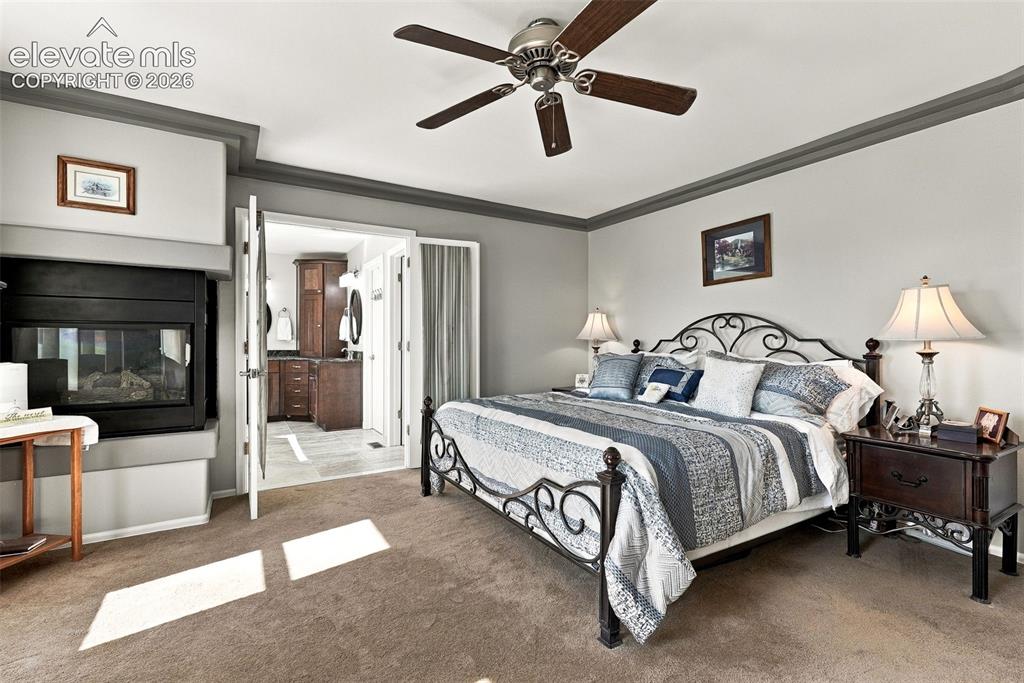 Image 19 of 50: Carpeted bedroom with a ceiling fan, a built-in fireplace, and double-door