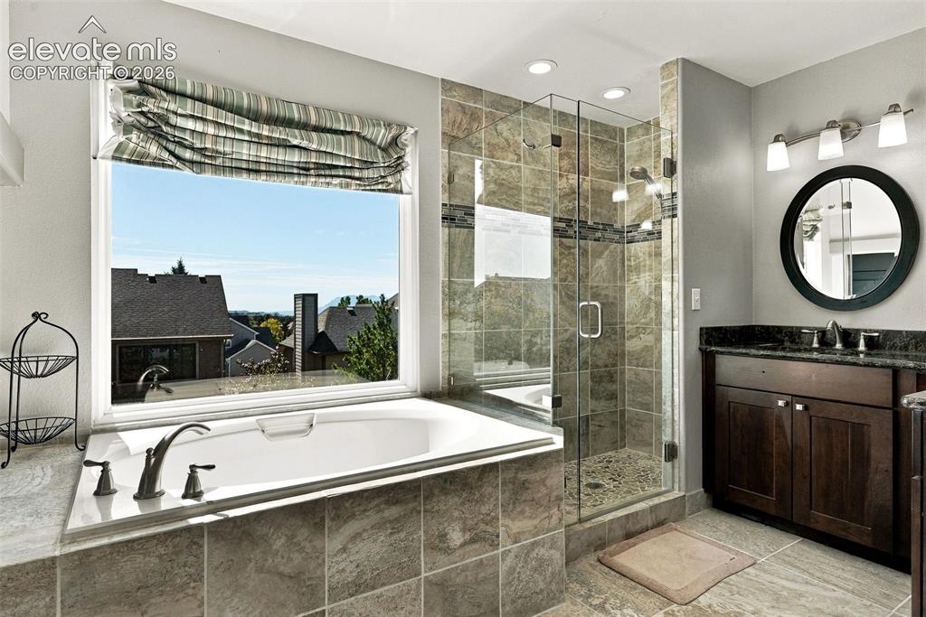 Image 24 of 50: Deep soaking tub with a tiled surround, glass-enclosed shower with stone ti