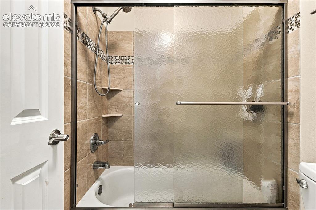 Image 28 of 50: Bathtub with a tiled surround, integrated shower, and textured glass slidin