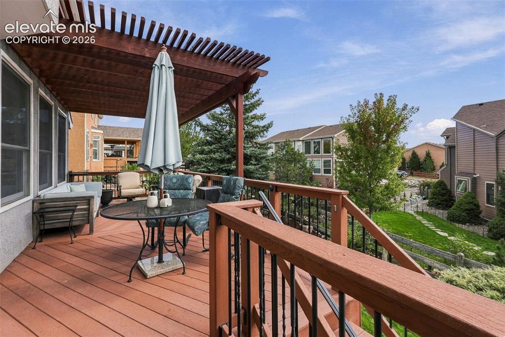 Image 45 of 50: Expansive wood-finish deck with a pergola, black metal railings, and a stuc