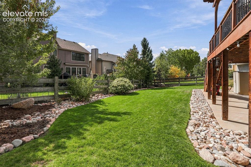 Image 47 of 50: Expansive green lawn with a rock-lined border, bordered by a wooden fence