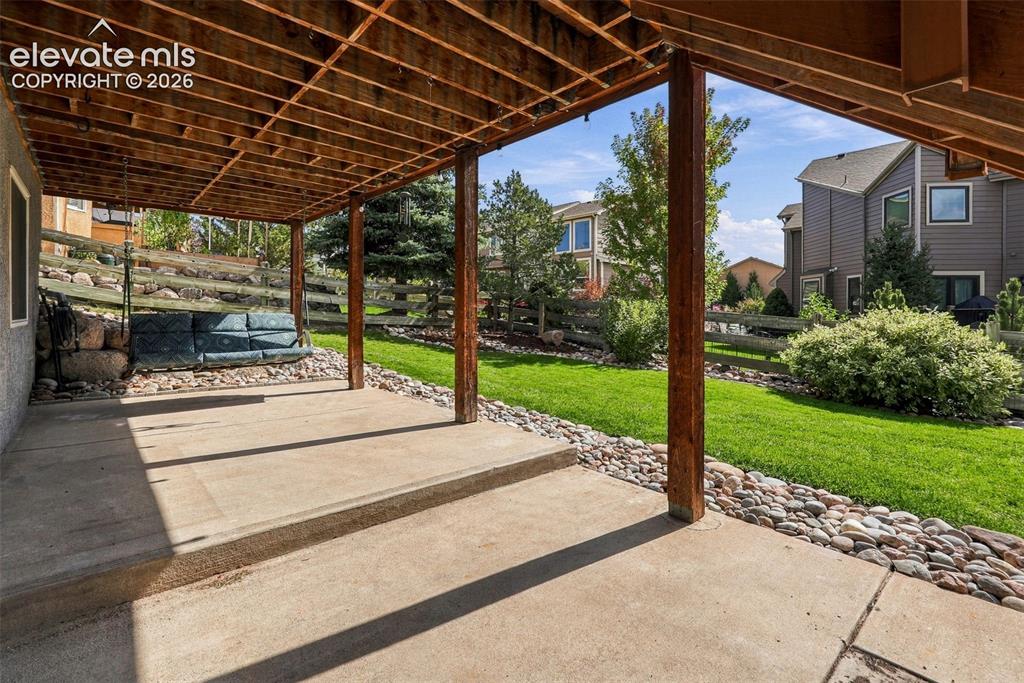 Image 48 of 50: Covered concrete patio with wood support posts and exposed wood ceiling joi