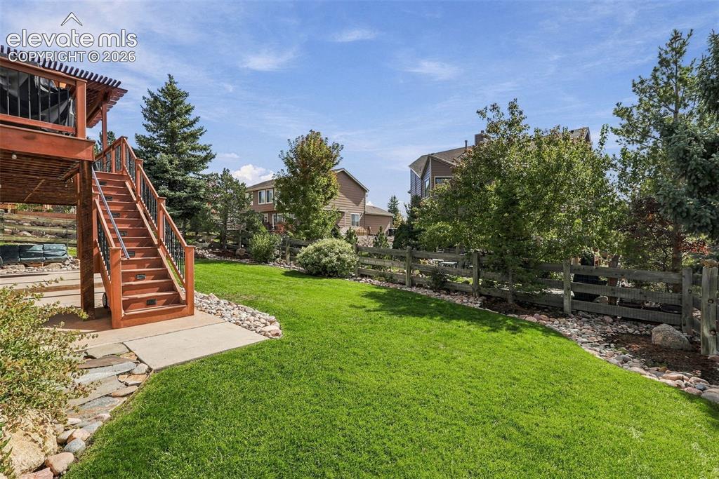 Image 49 of 50: Expansive lawn area, multi-tiered wooden deck, wrought iron stair railing,