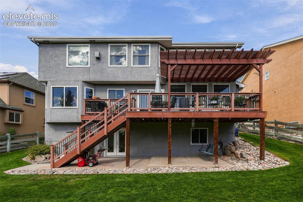 Image 50 of 50: Expansive two-story deck with a wooden pergola, leading to a ground-level p