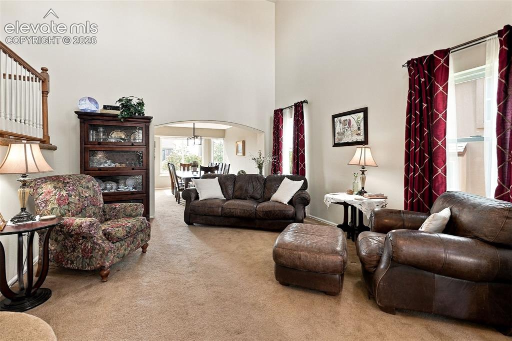 Image 7 of 50: Carpeted living area with vaulted ceilings, large windows, and an arched en