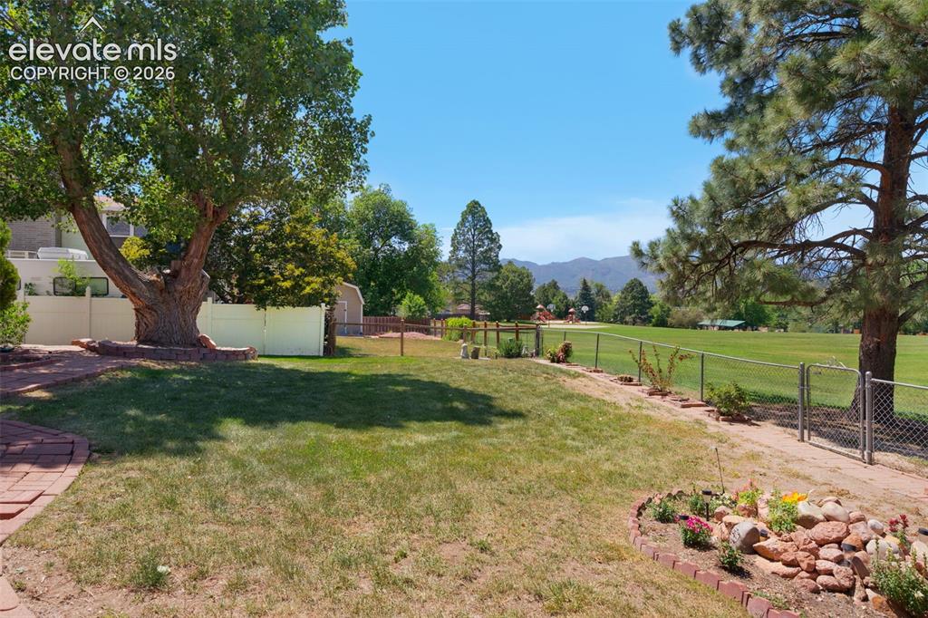 Image 19 of 25: Expansive backyard featuring a manicured lawn, established trees, and a bri