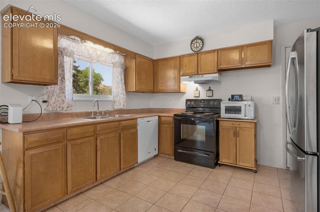 Image 6 of 25: Kitchen featuring wood cabinetry, tile flooring, a double basin sink, and a
