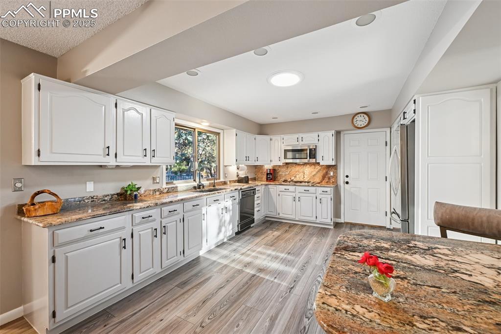 Image 21 of 48: Kitchen with dark stone countertops, decorative backsplash, white cabinets,