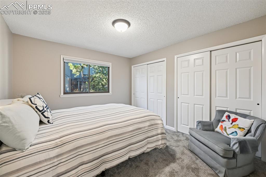 Image 28 of 48: Bedroom with two closets, carpet, and a textured ceiling