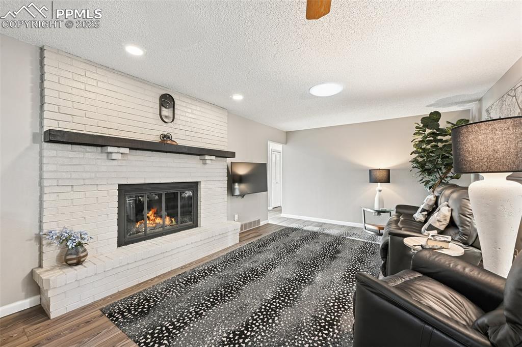 Image 3 of 48: Living area with a textured ceiling, luxury vinyl floors, a brick gas firep