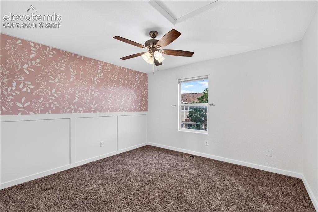 Image 17 of 28: Wall paneling with a patterned accent wall, ceiling fan, and carpeted floor