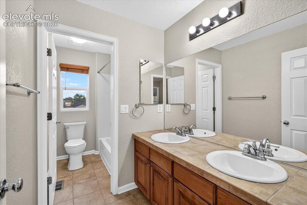 Image 18 of 28: Dual vanity with integrated sinks, wood-finish cabinetry, tile countertop, 