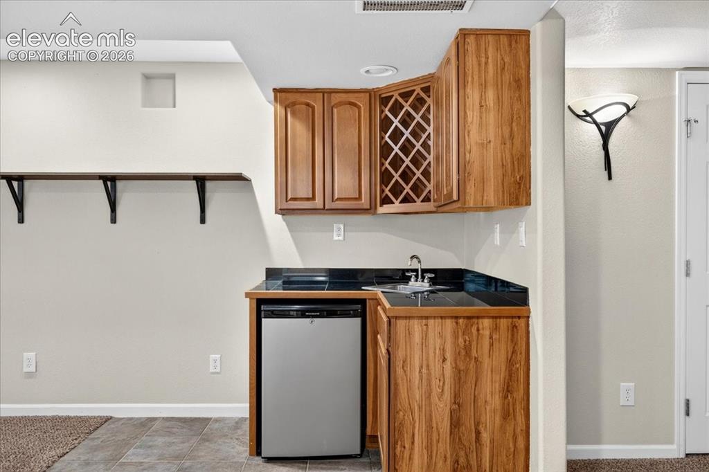 Image 21 of 28: Compact wet bar featuring wood-finish cabinetry, integrated wine rack, and 
