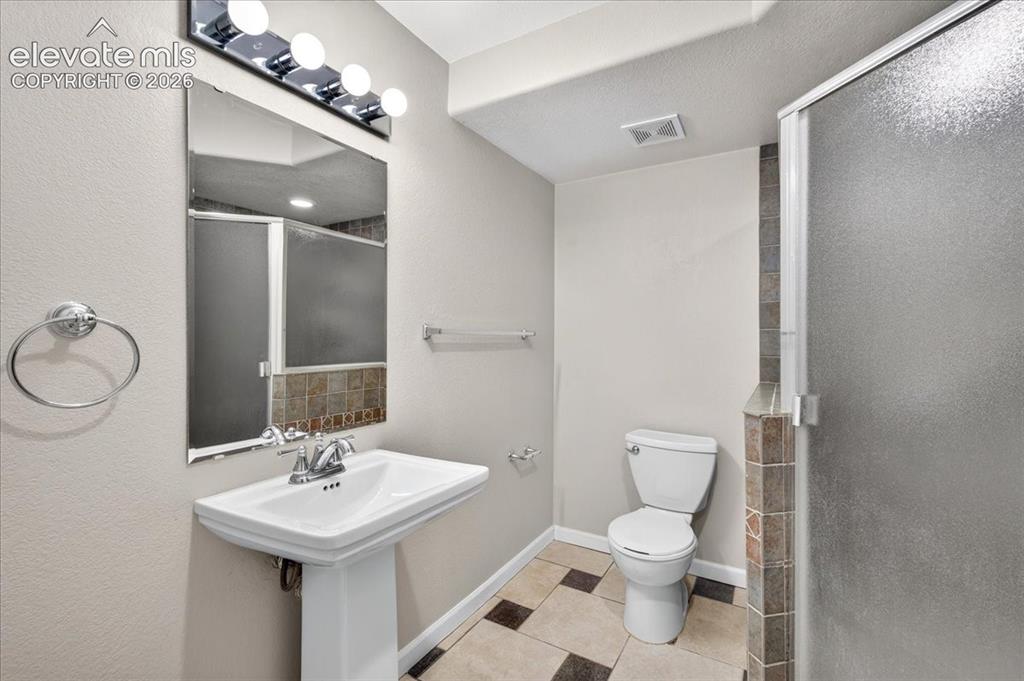 Image 24 of 28: Pedestal sink with chrome faucet, vanity lighting, tile flooring, and frost