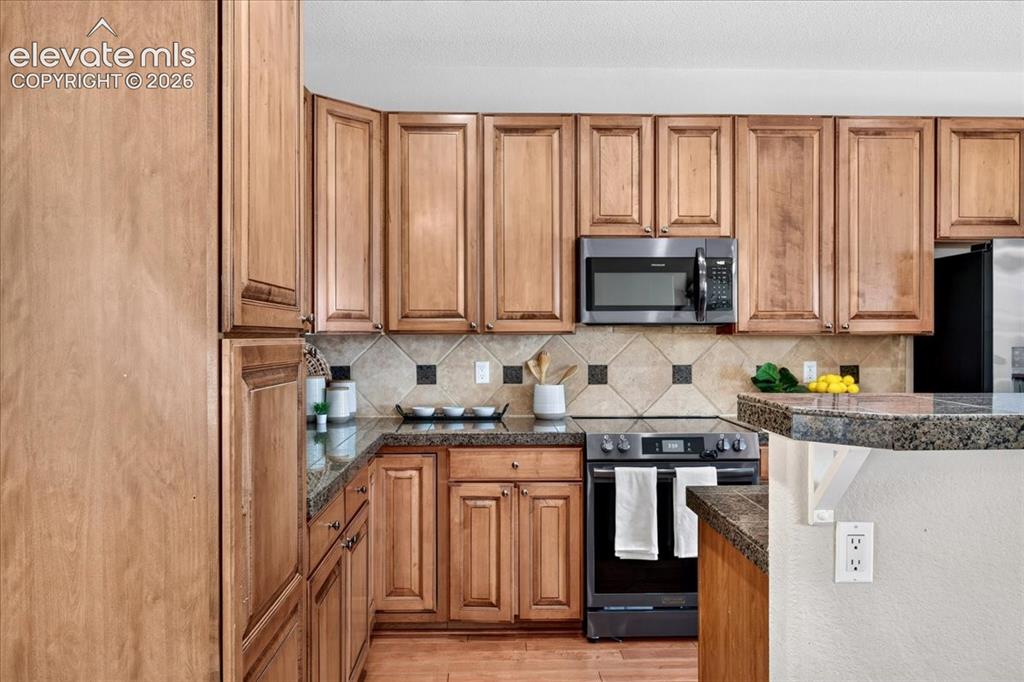 Image 8 of 28: Wood-finish cabinetry, granite-style countertops, tile backsplash with acce