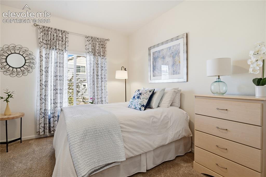 Image 24 of 47: Carpeted bedroom with a single window featuring blinds and decorative curta