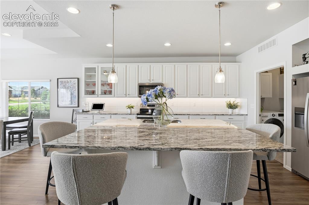 Image 7 of 47: Spacious kitchen featuring a large stone-finish island with seating, white 