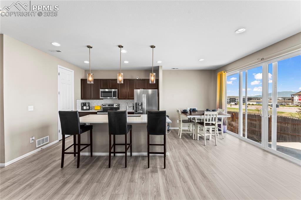 Image 10 of 32: Kitchen with dark brown cabinets, an island with sink, pendant lighting, ba