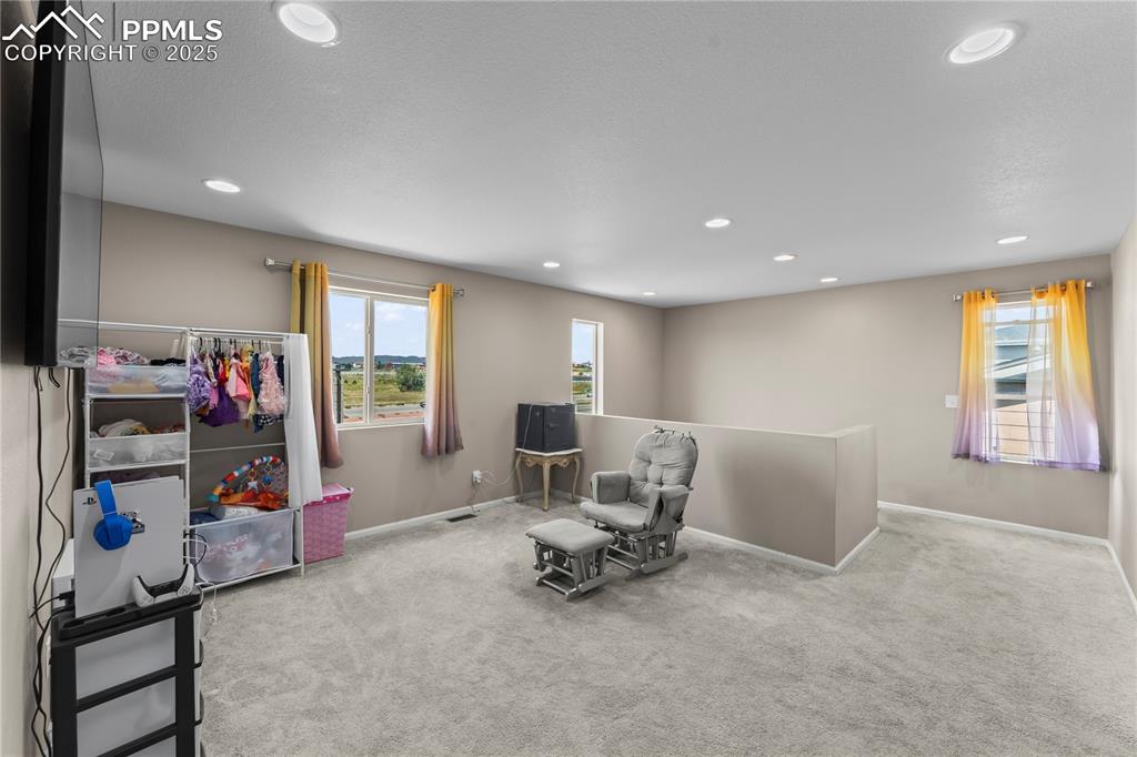 Image 16 of 32: Living area with light carpet, recessed lighting, and an upstairs landing