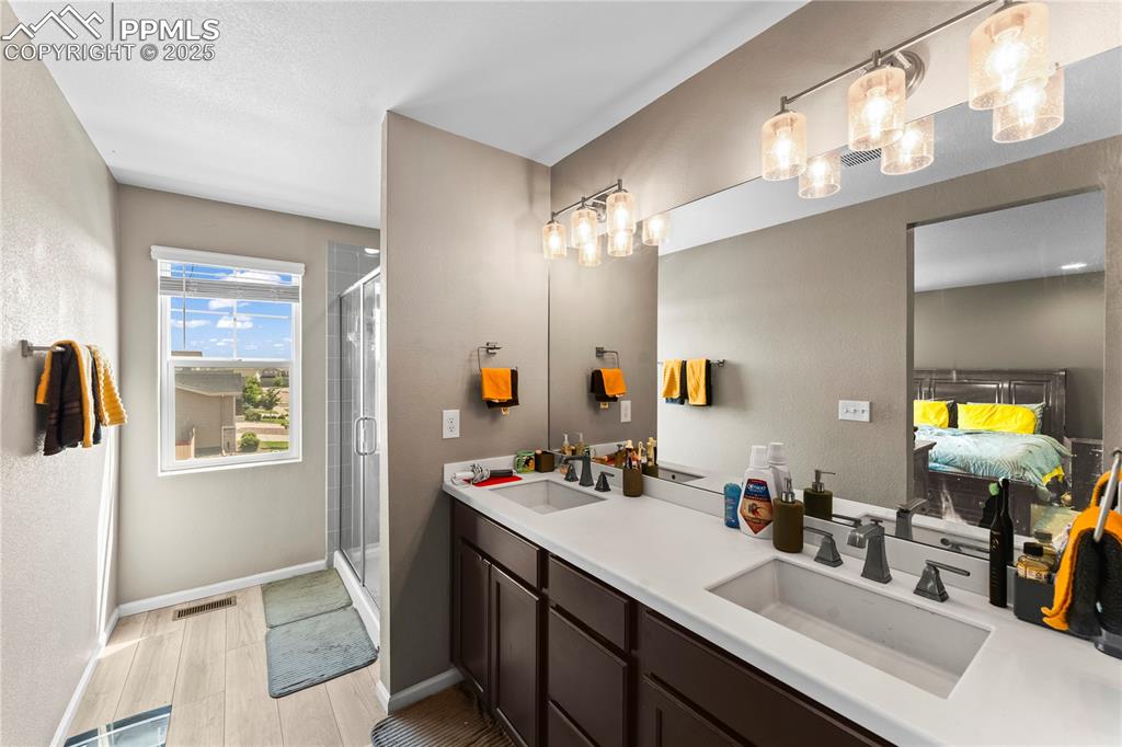 Image 19 of 32: Ensuite bathroom featuring double vanity, a shower stall, and light wood-ty
