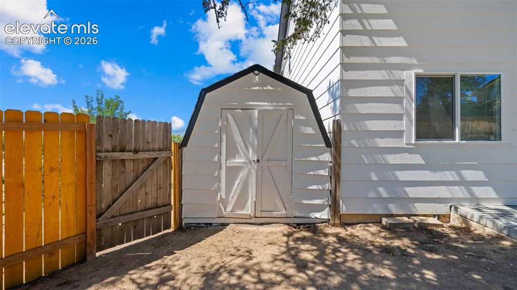 Image 31 of 44: White exterior siding with a shed, a wooden fence, and a window